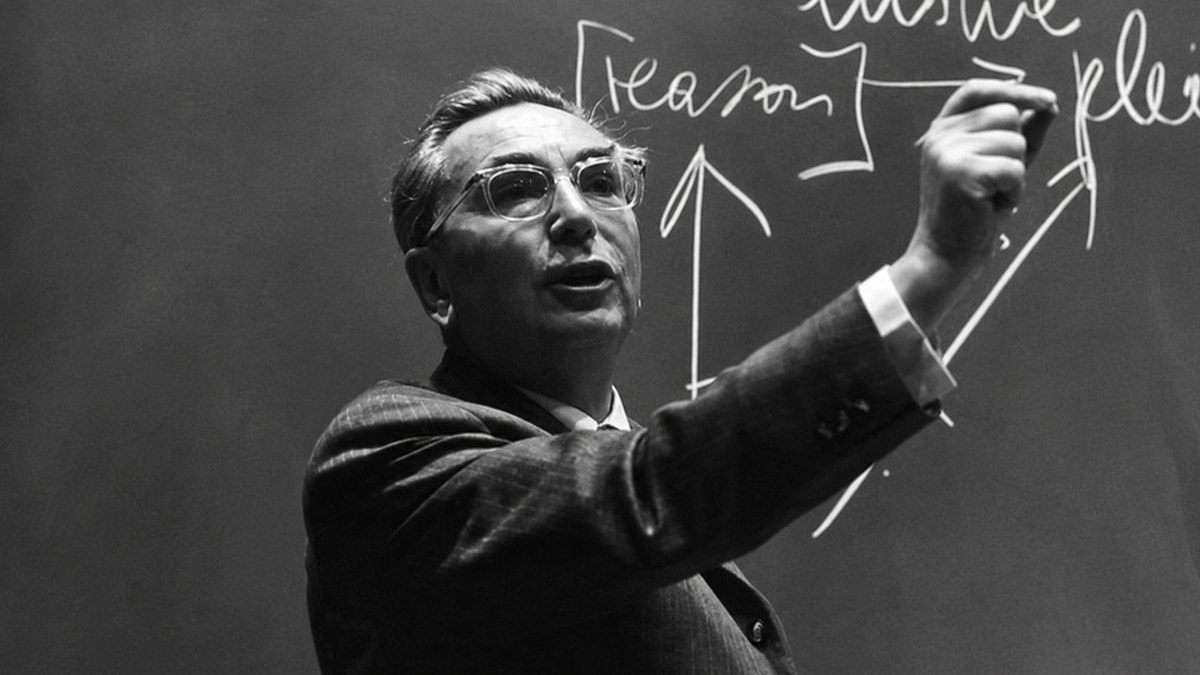 Viktor Emil Frankl, mais jovem, de terno, escrevendo num quadro-negro durante uma aula