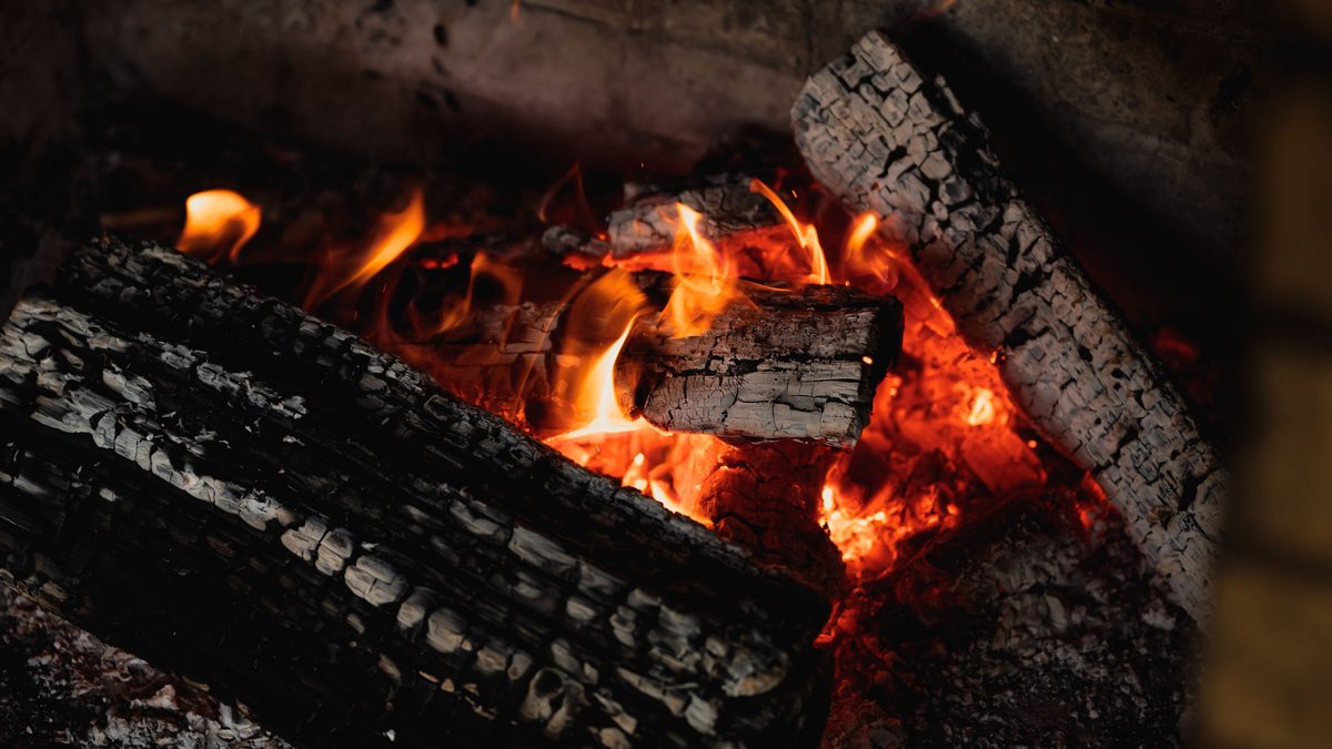 Lenha em brasa numa lareira acesa, chamas alaranjadas entre toras carbonizadas